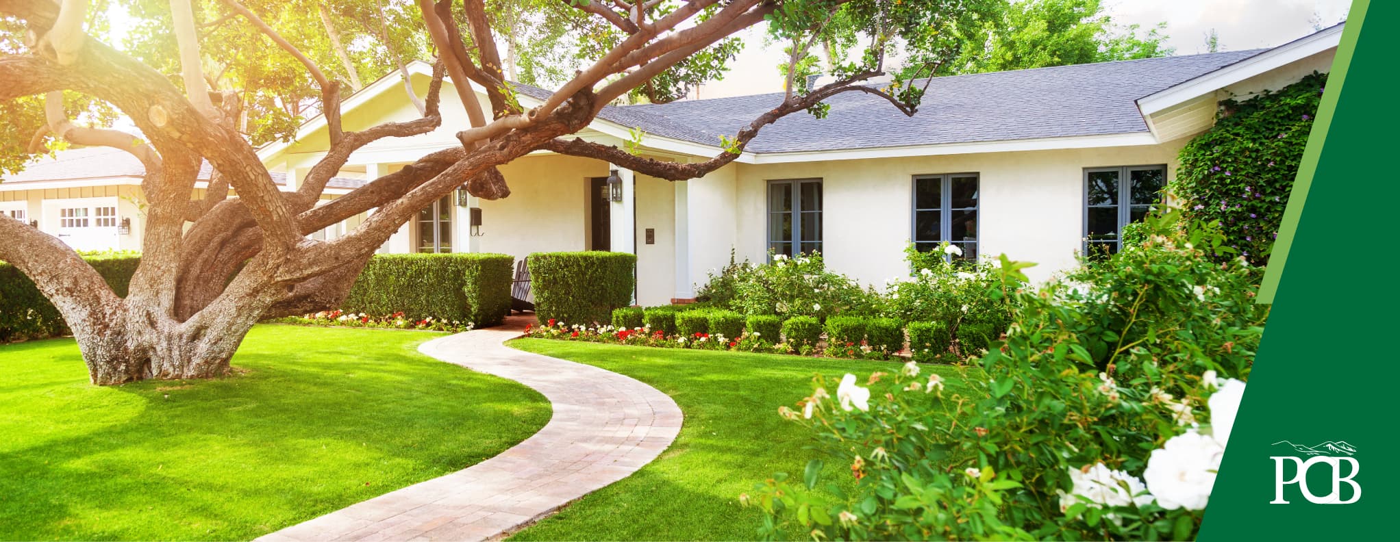 white rambler home with a winding sidewalk to the door. The lawn is cut perfectly and there is a big tree in front of the home. 