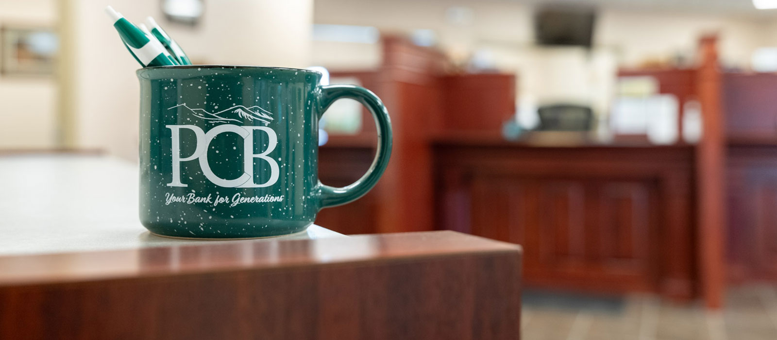 green PCB mug with pens and a table